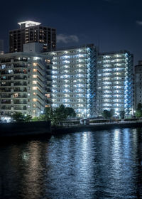 Illuminated buildings by river against sky at night