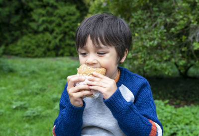 Close-up of boy eating food against plants in park