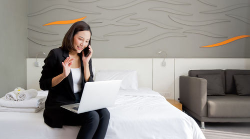 Young woman using mobile phone while sitting on bed
