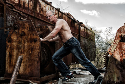 Full length of shirtless man on wood against sky