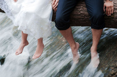 Low section of man and woman sitting on tree trunk in water