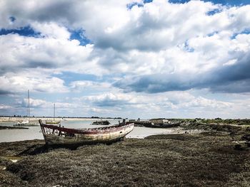 Old boat moored on beach against sky