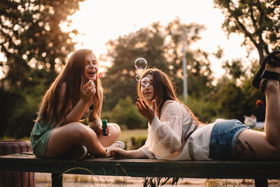 Happy lesbian couple playing with bubbles relaxing in park in summer