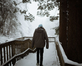 Rear view of woman walking on snow covered boardwalk during winter