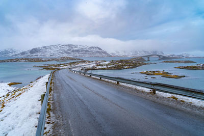 Road by snow covered land against sky