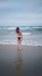 Woman in bikini standing at beach against sky