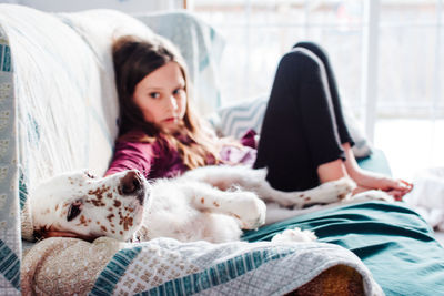 Cute girl with dog leaning on sofa at home