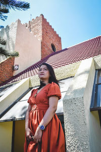 Portrait of young woman standing against building