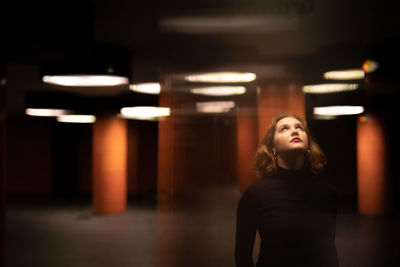 Young woman looking away while standing in illuminated room