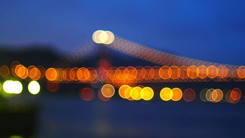 Defocused image of illuminated bridge against sky at night