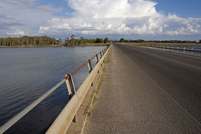 Empty road by railing against sky