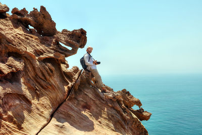 Man on rock by sea against clear sky