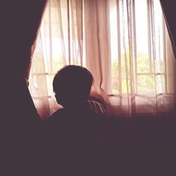 Rear view of woman looking through window at home