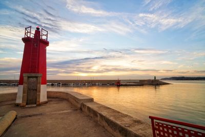 Lighthouse by sea against sky during sunset