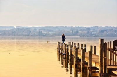 Woman standing on pier over sea against sky