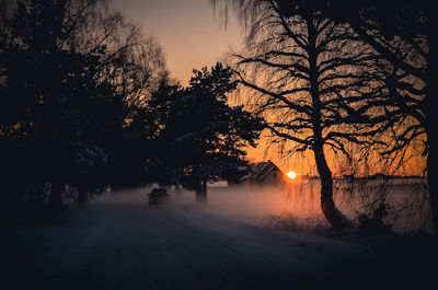 Silhouette trees on snow covered landscape during sunset