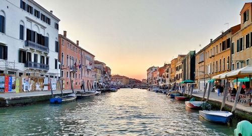 Boats moored in canal amidst buildings in city against sky