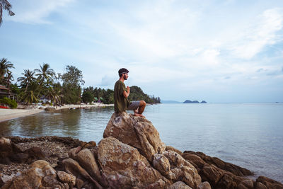 Man sitting on rock by sea against sky