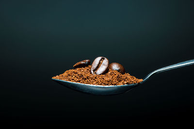 Roasted coffee beans and ground coffee on a spoon isolated on black background