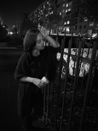 Full length of woman standing by railing in city at night