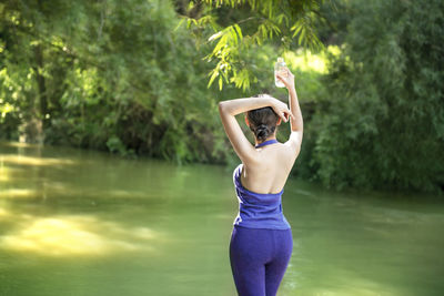 Rear view of woman standing by lake against trees