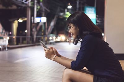 Side view of woman using smart phone while sitting on footpath