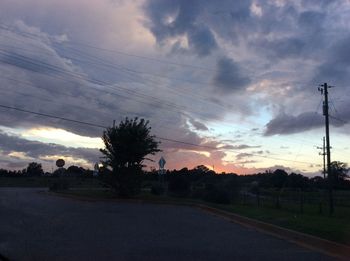 Silhouette of trees on landscape against cloudy sky