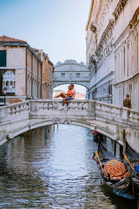 Couple sitting on bridge railing over canal in city