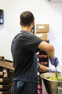 Side view of young male chef preparing food in container at restaurant commercial kitchen