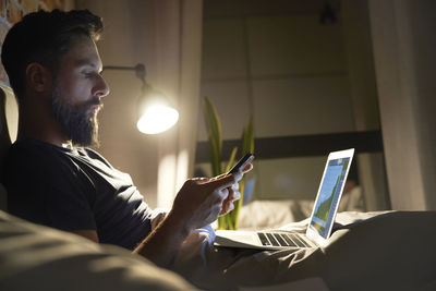 Side view of businessman using mobile phone while sitting by laptop