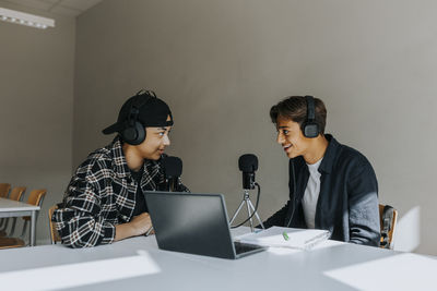 Smiling male students looking at each other during podcasting in classroom