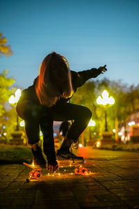 Young woman skateboarding on footpath against sky at night