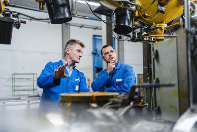 Male technicians wearing protective eyewear discussing on machinery equipment in factory