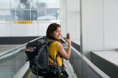 Portrait of cheerful woman using phone on moving walkway at airport