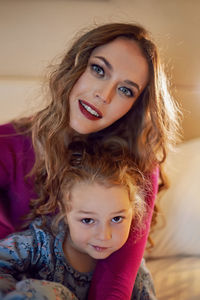 Mother in purple clothes with a sad dissatisfied daughter in a dress is sitting on a bed in a hotel