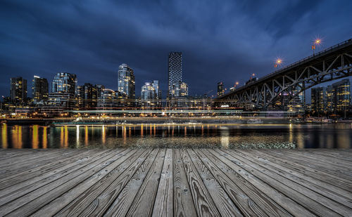 Illuminated bridge over river against buildings at night