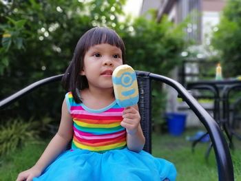 Girl looking away while holding popsicle on chair