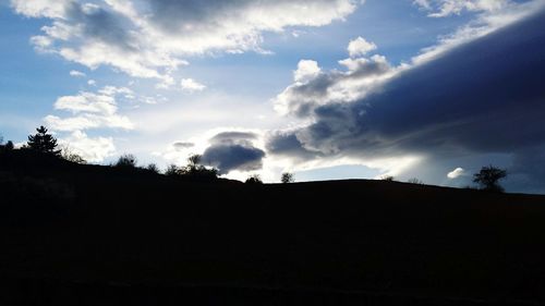 Silhouette of trees on landscape against cloudy sky