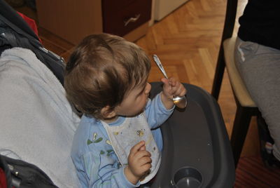 Side view of cute boy holding spoon on baby stroller at home