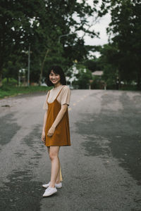 Full length portrait of a smiling young woman walking on road