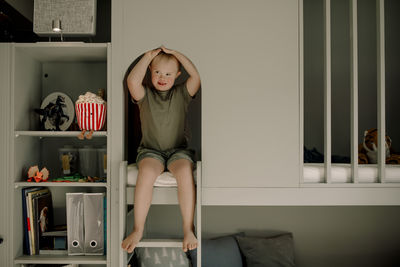 Full length of boy with down syndrome sitting on bunkbed ladder at home