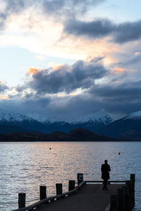 Man standing by lake against sky during sunset