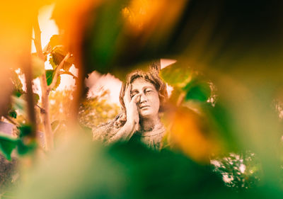 Old statue of aweeping stone angel on background of green leaves