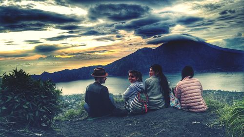 Rear view of people sitting on mountain against sky