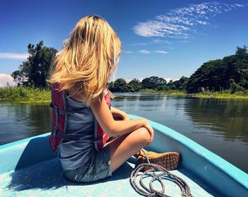 Side view of woman sitting on boat in lake against sky