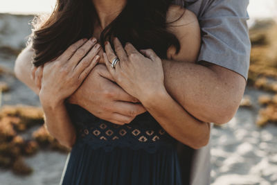 Arms and hands detail image of husband embracing wife from behind