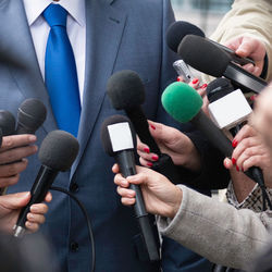 Cropped hands of journalists holding microphones in front of businessman