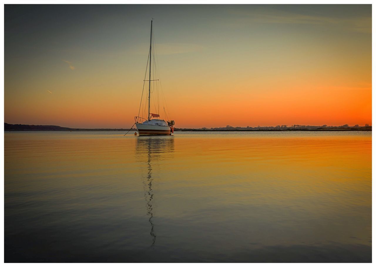 SAILBOATS MOORED IN SEA AGAINST SKY DURING SUNSET