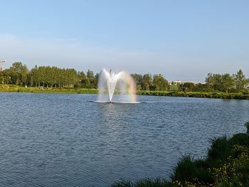 Fountain against lake and trees against sky