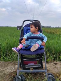 Girl sitting on field against sky